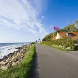 Droga nad morzem, domy z norweską flagą. Idealne miejsce na wycieczkę rowerem na Bornholm, warto sprawdzić koszty.