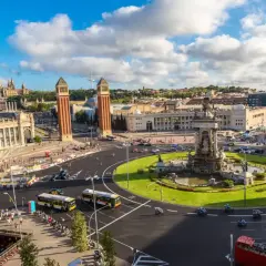 Plac Hiszpański w Barcelonie, z dwoma wieżami w tle i fontanną pośrodku. Ruch uliczny, autobusy i motocykle tworzą tętniącą życiem scenę w tym pięknym, **starym mieście Barcelona**.