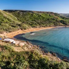 Malta's Riviera Beach: piaszczysta plaża, turkusowa woda i zielone wzgórza tworzą idylliczny krajobraz.
