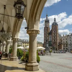 Urokliwy **Kraków Stary Miasto** z Sukiennicami i Kościołem Mariackim w tle. Widać kawiarniane stoliki pod arkadami.