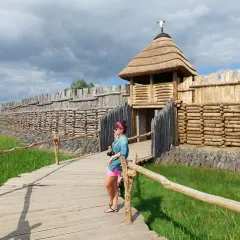 Kobieta na drewnianym pomoście podziwia rekonstrukcję grodziska, pokazującą, gdzie leży Biskupin.