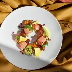 Talerz z łososiem, awokado, pomidorkami i nachos na złotym tle.