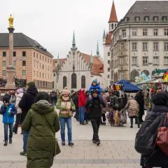 Tłum ludzi na placu w Niemczech, gdzie liczba ludności jest wysoka. W tle zabytkowe budynki i pomnik.