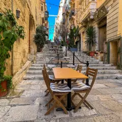 Malta sierpień: kamienne schody i stoliki kawiarniane w wąskiej uliczce, idealne na letni wieczór.