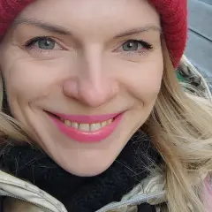 Uśmiechnięta blondynka w czerwonej czapce i złotej kurtce, jakby właśnie spacerowała po ulicach Czech, gdzie ludność cieszy się zimową aurą.