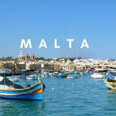 Malta we wrześniu: kolorowe łodzie luzzu kołyszą się na lazurowej wodzie, w tle malownicze miasteczko. Idealna pogoda na podróż.