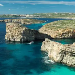 Malta zima: turkusowe wody, skaliste klify i łodzie kołyszące się na falach. W oddali widać miasto.