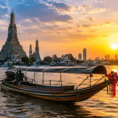 Łódź płynie po rzece w stronę Wat Arun, symbolu Bangkoku, podczas zachodu słońca.