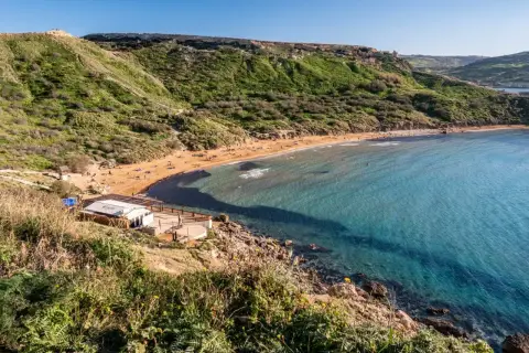 Malta's Riviera Beach: piaszczysta plaża, turkusowa woda i zielone wzgórza tworzą idylliczny krajobraz.