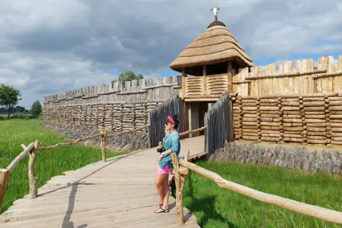 Kobieta na drewnianym pomoście podziwia rekonstrukcję grodziska, pokazującą, gdzie leży Biskupin.