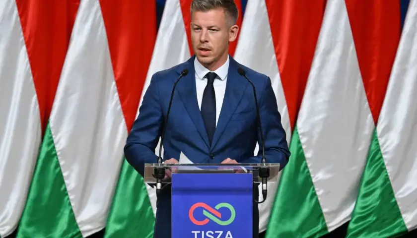 Mężczyzna w garniturze przemawia na tle flag Węgier. Dyskusja o węgry liczba ludności.