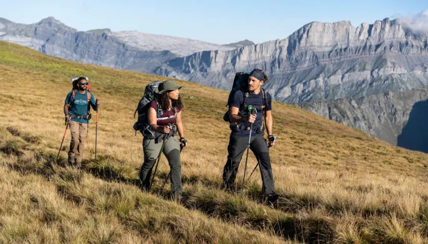 Trzech turystów z plecakami i kijkami przemierza górski szlak, przypominający **Pacific Crest Trail**.