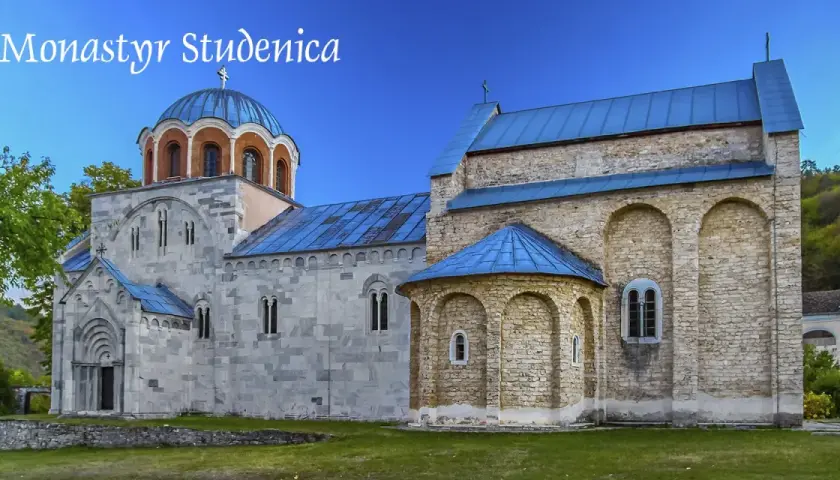 Kamienne mury i niebieskie dachy monastyru Studenica wznoszą się na tle zielonych wzgórz.