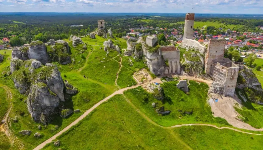 Ruiny zamku na skale, porośnięte zielenią, z widokiem na las i miasto.
