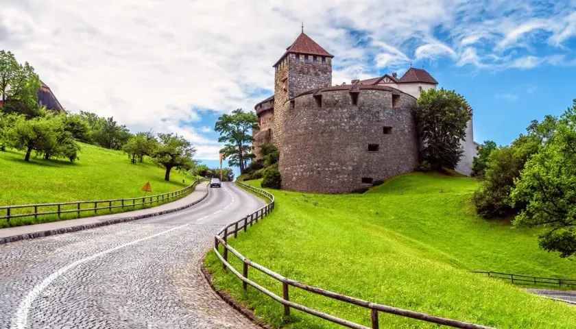 Droga wije się pod górę do zamku w państwie Liechtenstein, otoczonego zielonymi wzgórzami i drzewami.