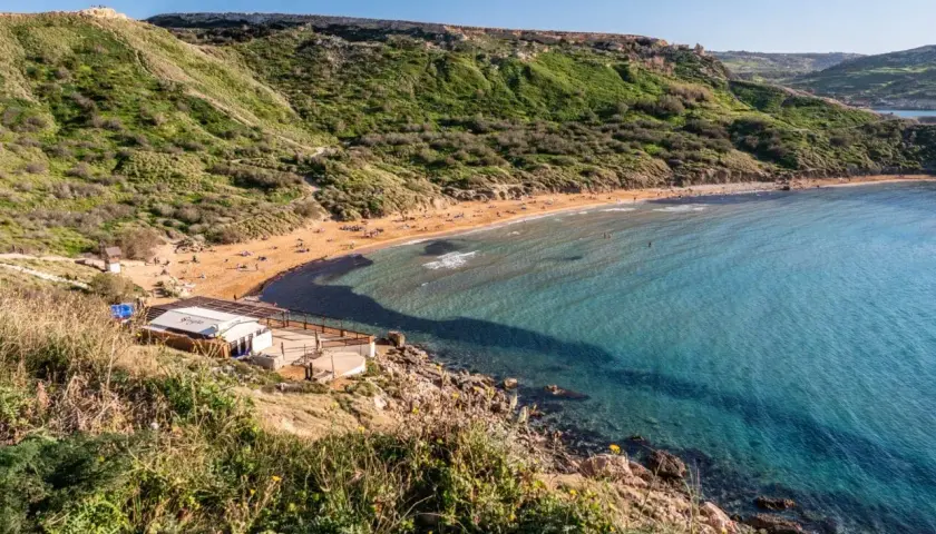 Malta's Riviera Beach: piaszczysta plaża, turkusowa woda i zielone wzgórza tworzą idylliczny krajobraz.
