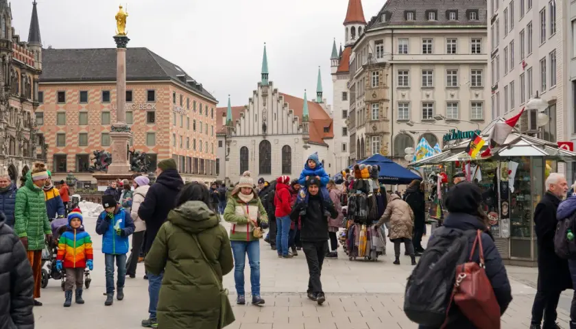 Tłum ludzi na placu w Niemczech, gdzie liczba ludności jest wysoka. W tle zabytkowe budynki i pomnik.