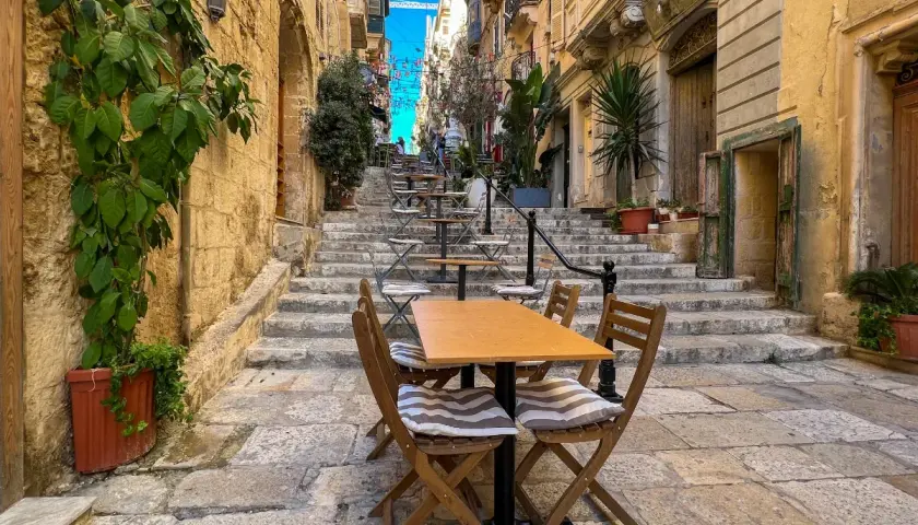 Malta sierpień: kamienne schody i stoliki kawiarniane w wąskiej uliczce, idealne na letni wieczór.