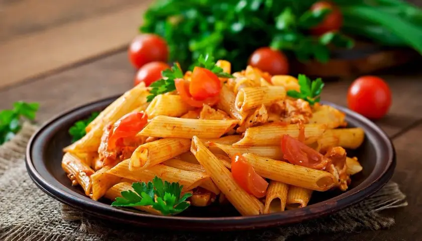 Penne z sosem pomidorowym i kurczakiem, ozdobione pomidorkami i natką pietruszki. Idealne pytanie: jakie wino do spaghetti?