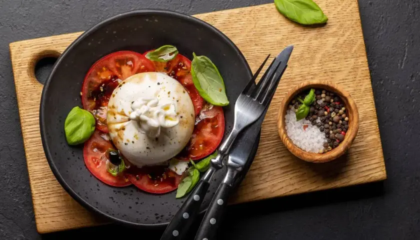Ser burrata z pomidorami i bazylią. Idealny sposób, jak jeść burratę: z pieprzem, solą i oliwą.