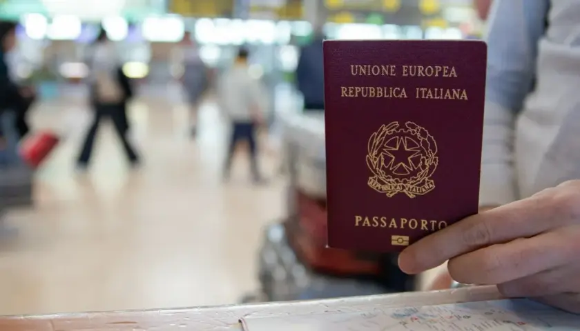 W podróży do Irlandii, czy do Irlandii potrzebny jest paszport? W ręku włoski paszport, na tle lotniska.