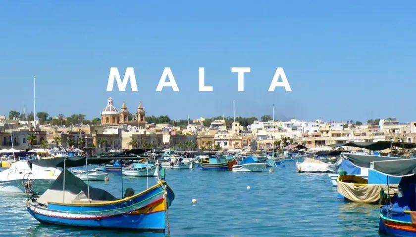 Malta we wrześniu: kolorowe łodzie luzzu kołyszą się na lazurowej wodzie, w tle malownicze miasteczko. Idealna pogoda na podróż.