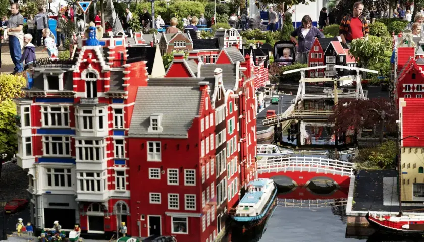 Miniaturowa holenderska zabudowa z kanałami i mostami w **Lego Land**. Ludzie spacerują wśród kolorowych budynków z klocków.