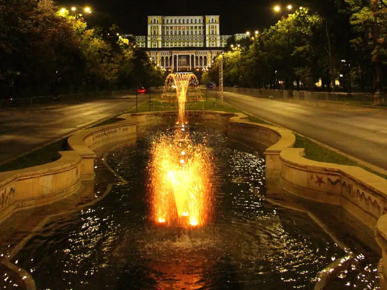 București, stolica Rumunii, nocą. Fontanna z rozświetlonymi strumieniami wody przed monumentalnym budynkiem.