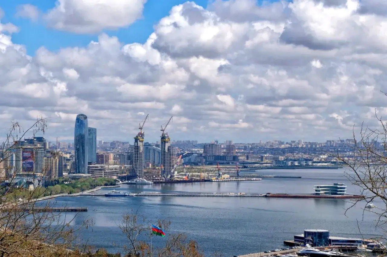 Widok na nowoczesne państwo z baku, z drapaczami chmur, dźwigami budowlanymi i flagą Azerbejdżanu na pierwszym planie.